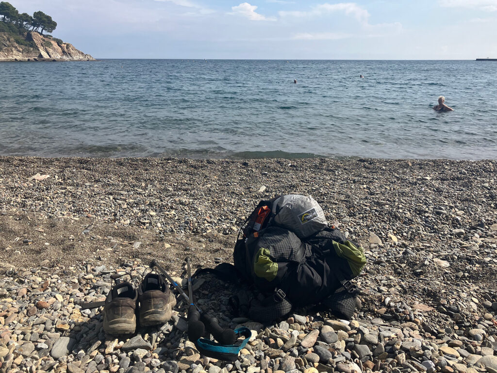 The stony beach of Banyls sur Mer with my backpack, shoes and walking sticks